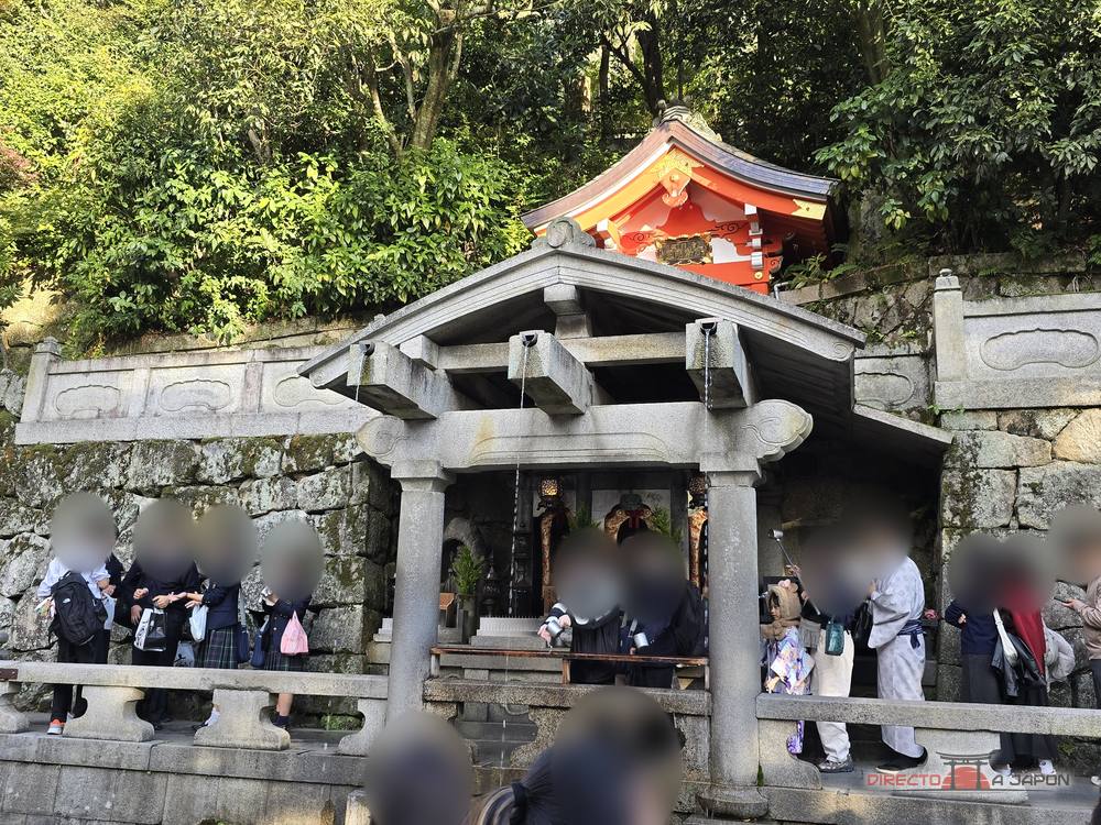Cascada Otowa de Kiyomizudera: tres chorros de agua caen bajo un tejadillo de piedra mientras los visitantes esperan con los cazos de mango largo.