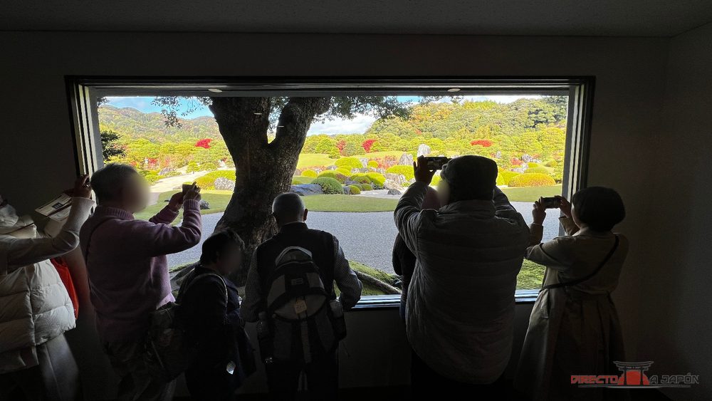 Visitantes fotografiando el jardín del Museo de Arte Adachi enmarcado por una ventana.