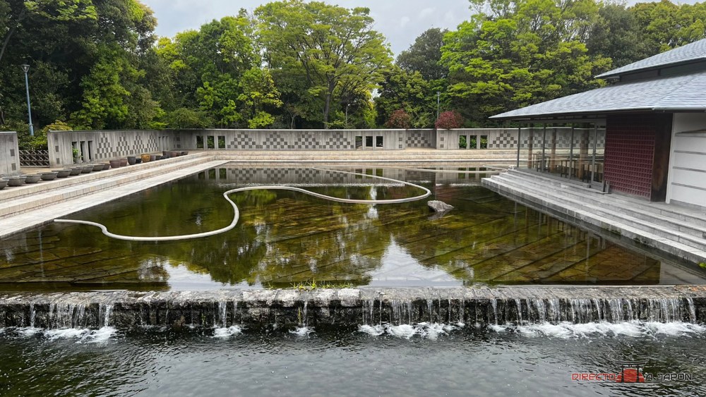 Cascada bajando a un estanque junto a un edificio tradicional, en el jardín Shirotori de Nagoya.